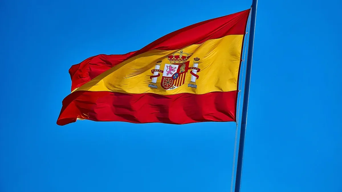 The Spanish flag, which is a rectangular flag with two horizontal stripes of red and yellow, featuring the national coat of arms in the cent